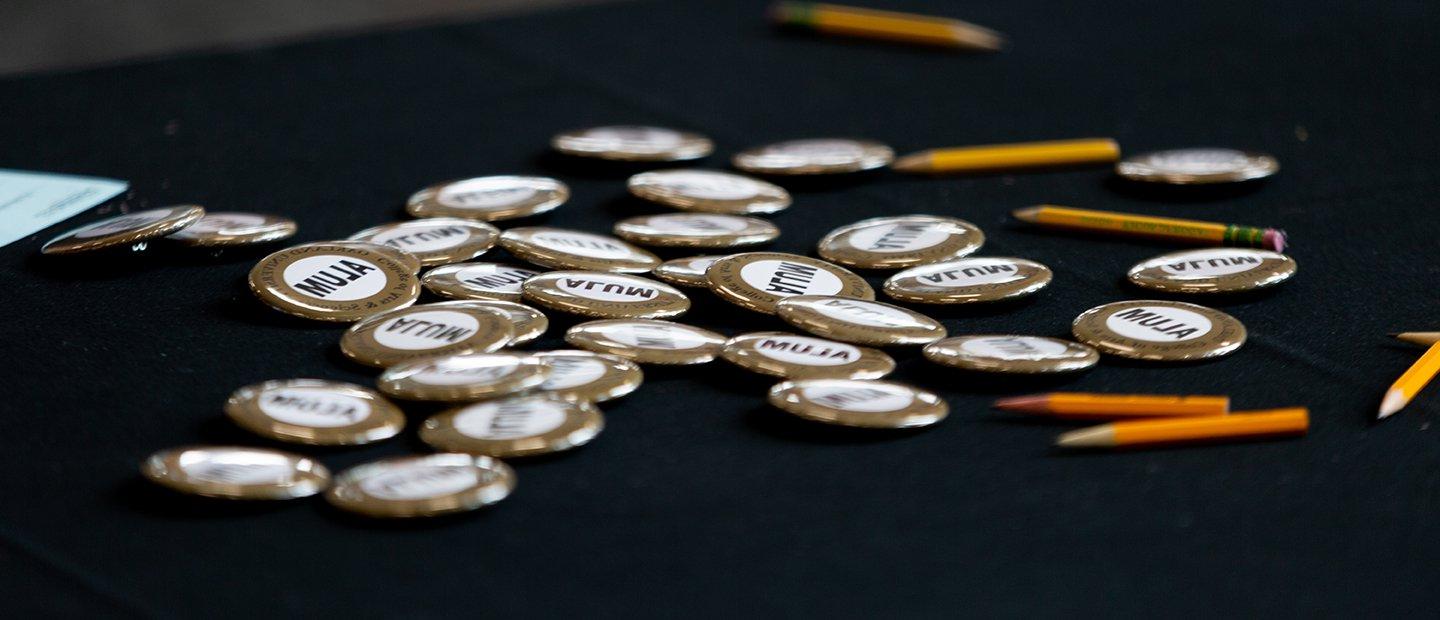 A bunch of round buttons that say Alum on them and a few pencils on a table.