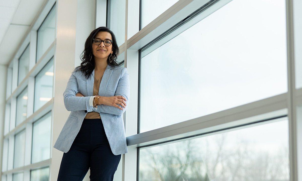 Woman standing in front of bank of windows, smiling, arms crossed.