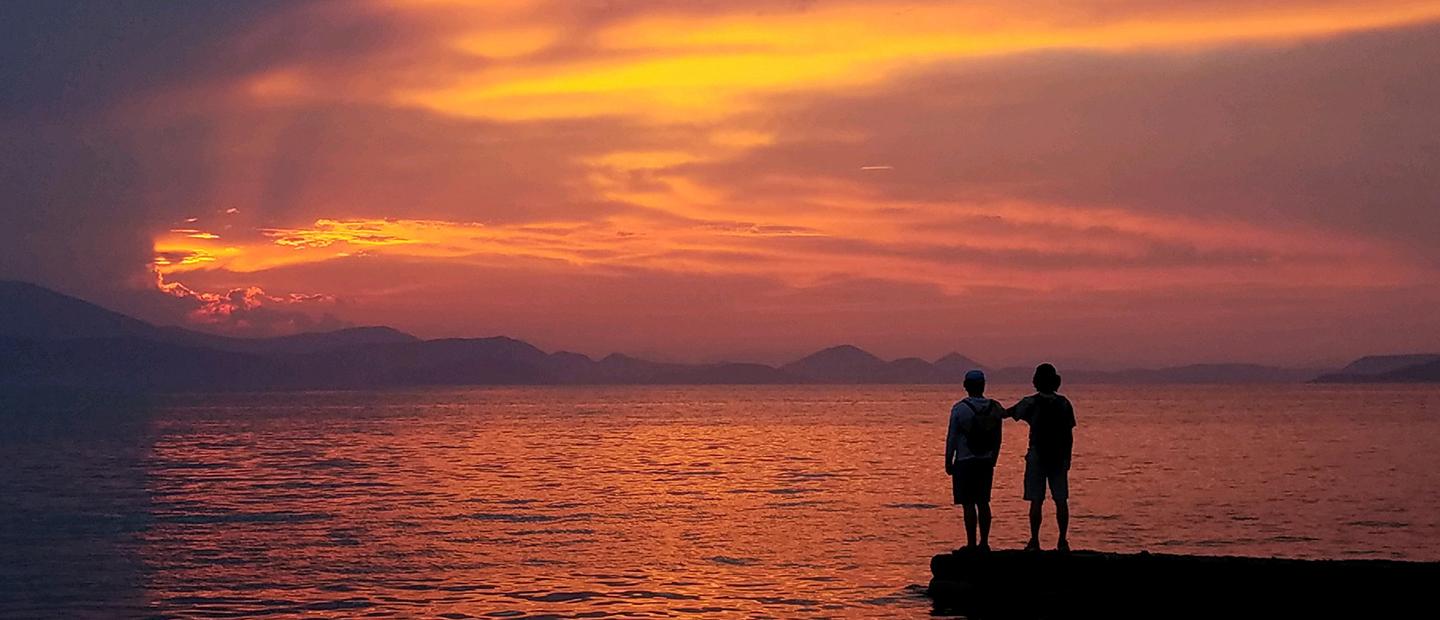 image of two people facing a sunset over a large body of water